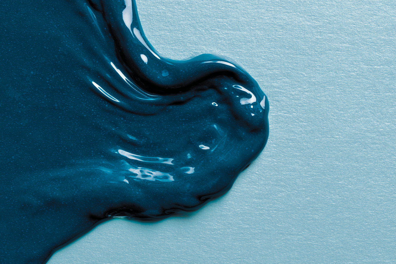 Glossy teal gel spreading across pale textured paper, editorial abstract