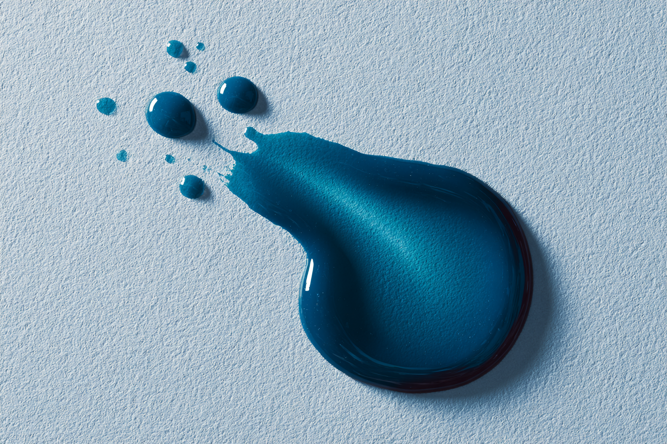 A teal droplet beside a soft spatter on pale paper, editorial abstract
