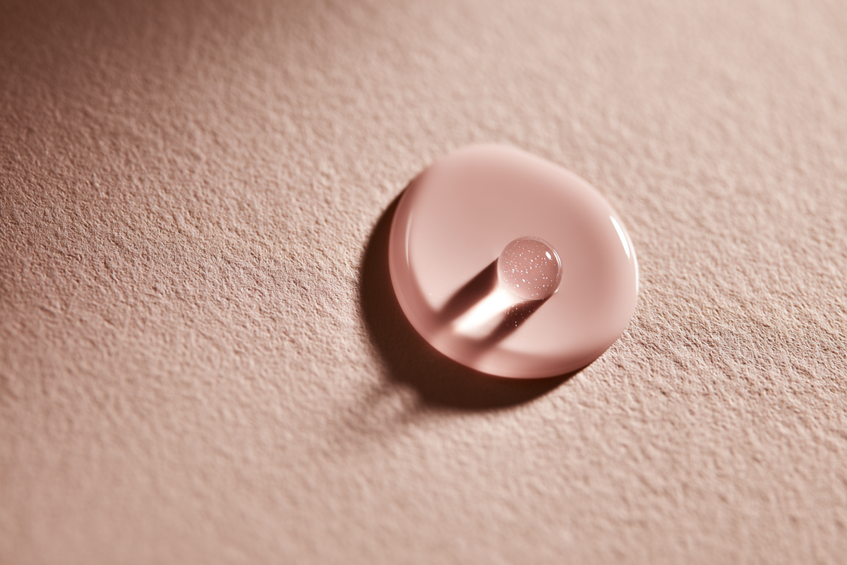 A single soft pink droplet on textured tan paper