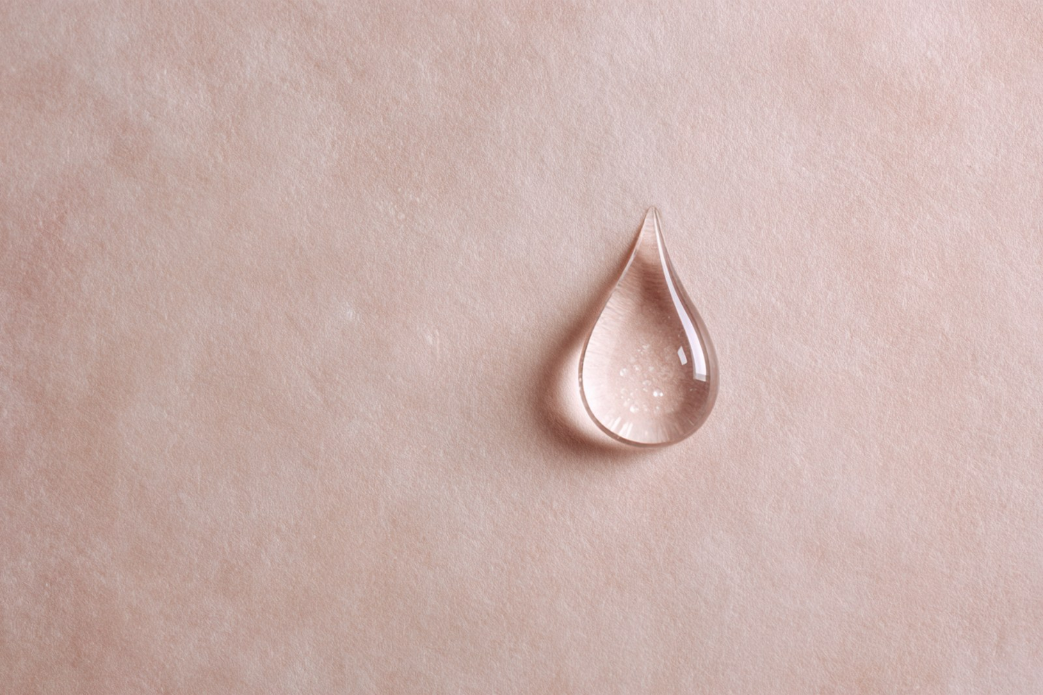 A single clear droplet on a soft blush surface