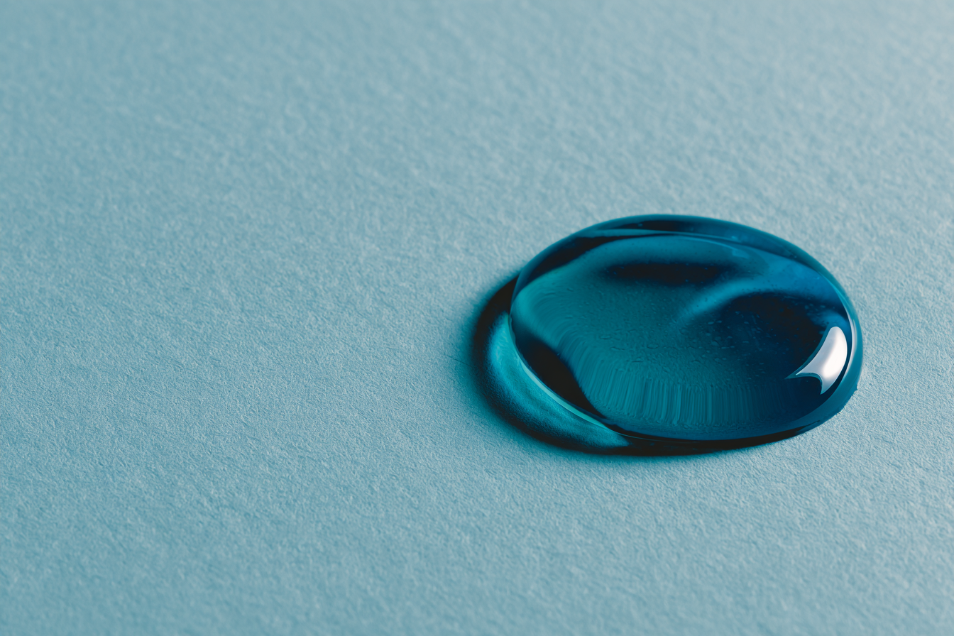 A single clean teal droplet resting on soft paper, editorial abstract