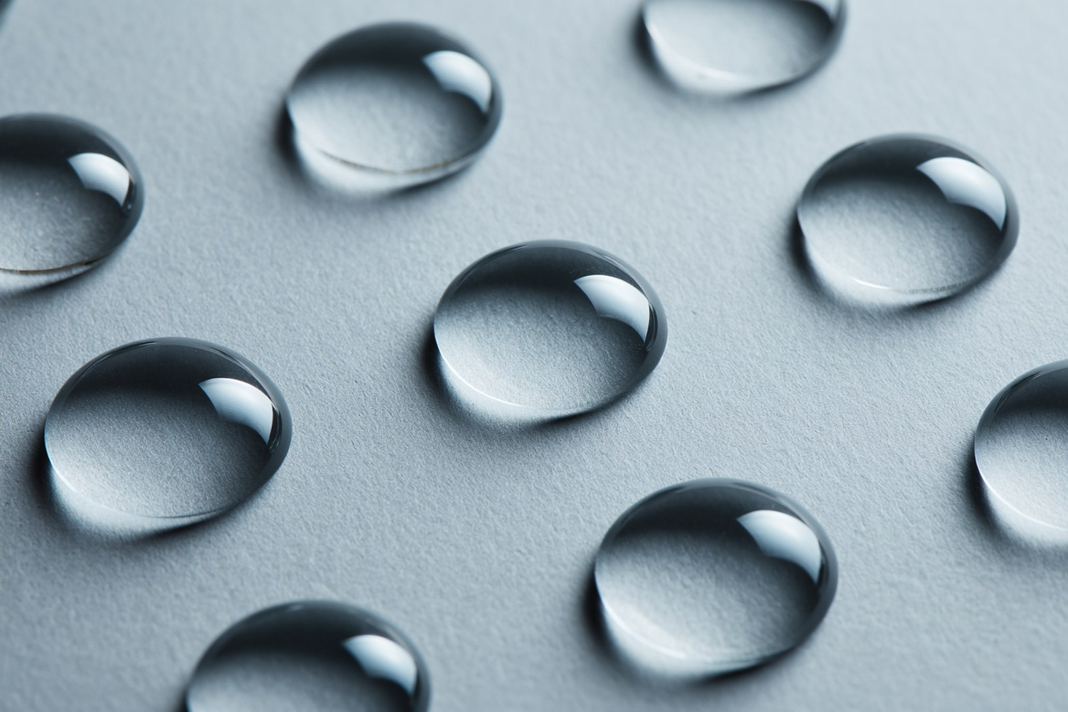 Evenly spaced identical clear droplets on a soft grey surface