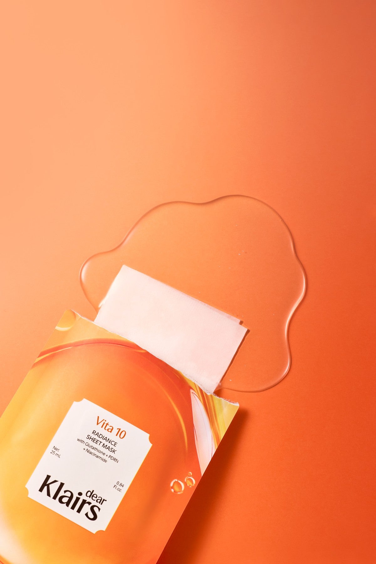 Dear Klairs Vita 10 Radiance Sheet Mask product with vitamin sheet texture and orange glow background
